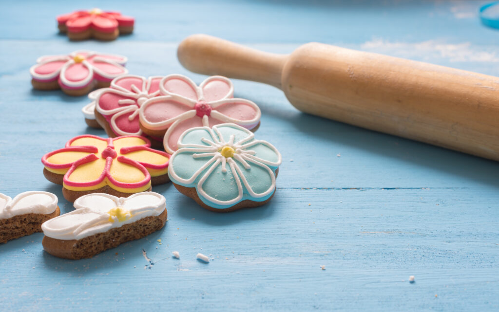 Flower shaped gingerbread cookies and rolling pin on a blue wooden table.