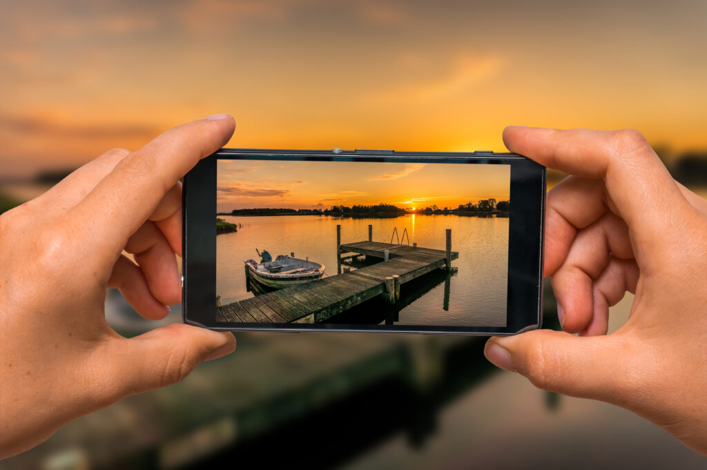 Woman hands with mobile cell phone to take a photo of sunset over lake in the Netherlands
