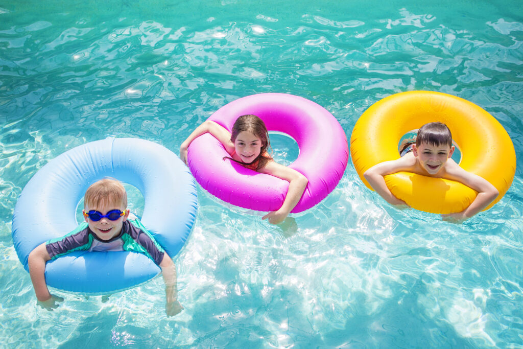 Group of cute kids playing on inflatable tubes in a swimming pool on a sunny day